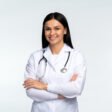 Portrait of beautiful young female doctor in white medical jacket isolated on white background. Brunette woman medic crossed hands and smiling at the camera